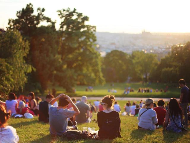 People relaxing on a sunlit park hill at sunset, distant city skyline.