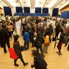 Crowded conference poster session in a large hall with attendees viewing displays.