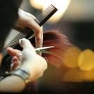 Hairdresser cutting client's red hair with comb and scissors in a salon.