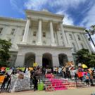 Domestic workers protest on the California Capitol steps with colorful signs and altar during the day.